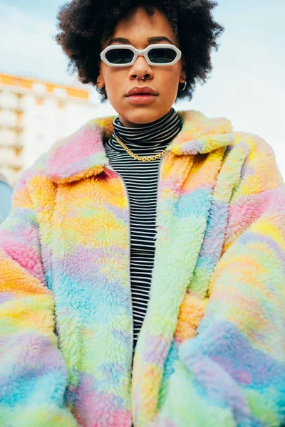 Genç siyah stil kıvırcık saçlı kadın dışarıda poz veriyor güneş gözlüğü takıyor.