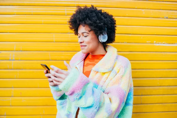 屋外で音楽を聴く楽しさを持つ若い黒人女性スマートフォンとエンターテイメントを楽しむワイヤレスヘッドフォン — ストック写真