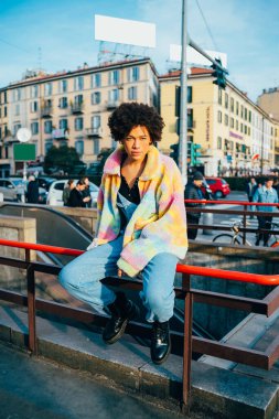 Genç, kendine güvenen, şık bir kadın. Kameraya bakıyor. Havalı, sakin ve kaygısız.