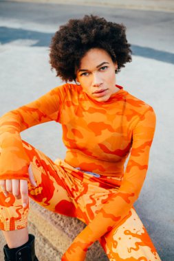 Güçlü ve gururlu genç kıvırcık siyah kadın, dışarıda poz veriyor kameraya bakıyor kendine güveni tam.