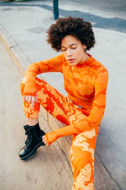 Genç siyah kıvırcık saçlı kadın dışarıda tasasız poz veriyor havalı tavırlar serin gözler kapalı