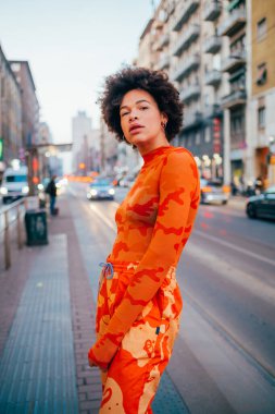 Kendine güvenen kıvırcık, siyah kadın dışarıda kameraya güçlü ve gururlu bir poz veriyor.