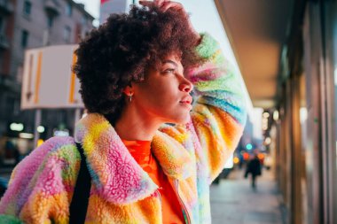 Genç kıvırcık saçlı siyah kadın gece vitrinlere bakıyor. 