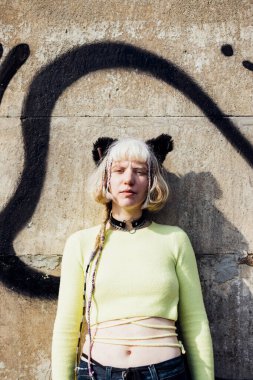 Dışarıda poz veren farklı, ikili olmayan kadın kameraya ciddi ve kendinden emin bakıyor.