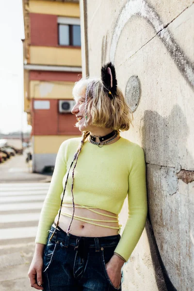 İkili olmayan genç bir kadın dışarıda gülüyor, olumlu duygular besliyor, havalı, uyumsuz kıyafetler giyiyor.