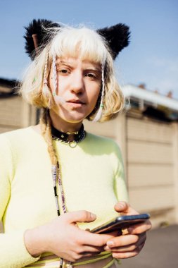 Genç, cinsiyeti değişken, açık havada akıllı telefon kullanan, kendine güvenen kameralı bir kadın. 