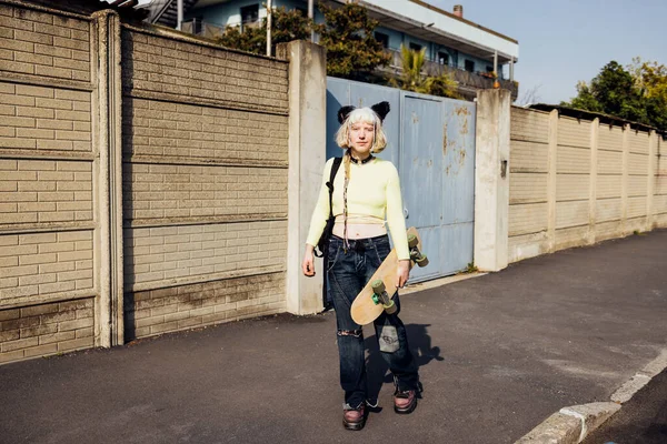 Young rebel gender fluid woman real beauty posing outdoors looking over holding skateboard