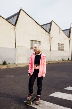 Gender fluid non conformist woman posing outdoor with skateboard