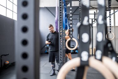 Two young sportive athletic friends indoors gym taking a break using smartphone drinking water