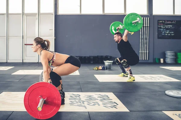 Man and woman weightlifting training indoors gym bodybuilding crouching using barbell