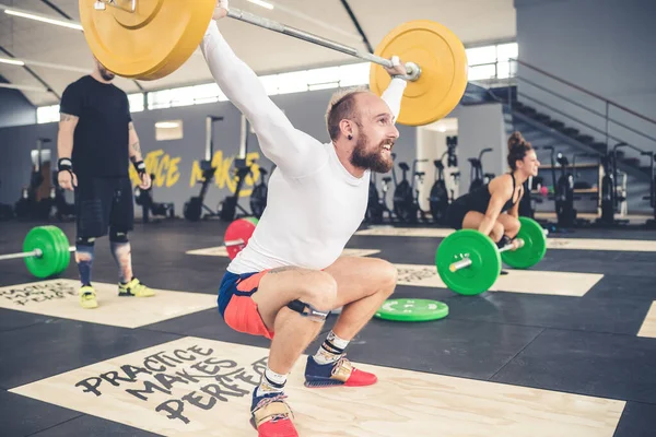 Young Sportive Muscular Man Weightlifting Indoors Gym Crouching Teammates — Stock Fotó