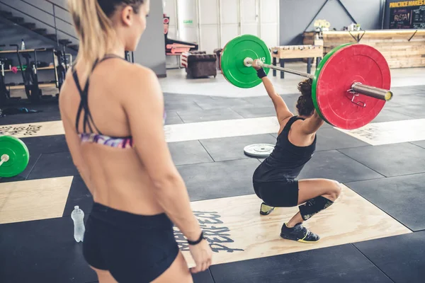 Coach assisting athlete while training indoor gym weightlifting crouching barbell weights