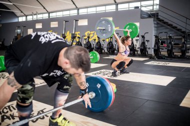 Young sportive athletic muscular woman indoors gym weight lifting crouching training 