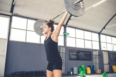 Spor salonundaki halterlerle egzersiz yapan genç bir kadın.