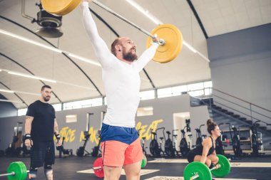 Kaslı atletik adam diğer insanlarla birlikte ağırlık kaldırma sınıfına katılıyor.