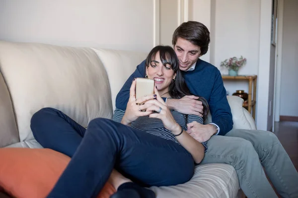 Sweet Young Couple Sitting Couch Hugging Using Smartphone Watching Video — Stock Photo, Image