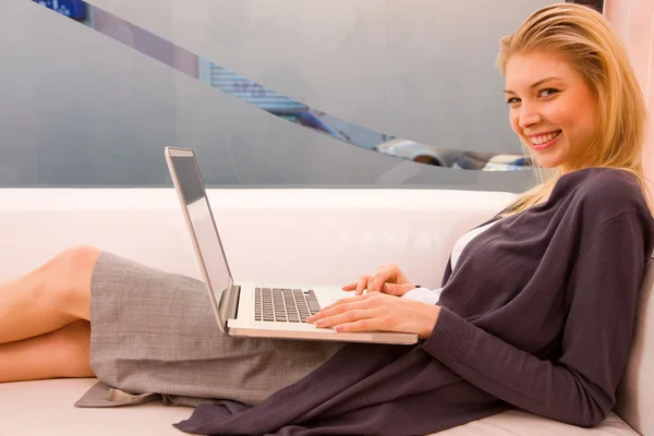 Smiling young woman using laptop sitting couch — Stock Photo, Image