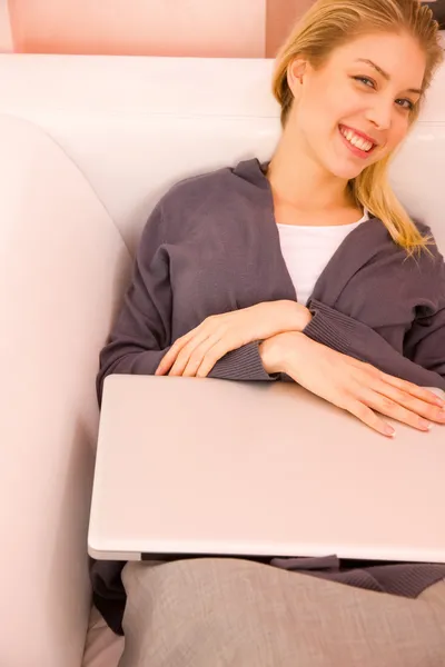 Sorrindo jovem mulher com laptop deitado sofá — Fotografia de Stock