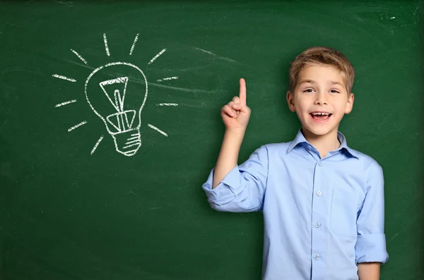 Schooljongen permanent in de buurt van blackboard met gloeilamp — Stockfoto