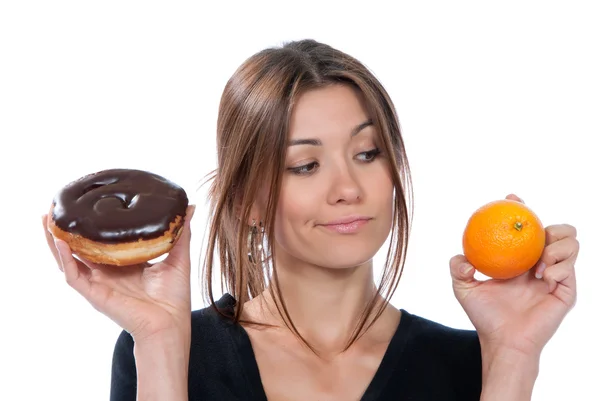 Vrouw vergelijken ongezonde donut en oranje fruit — Stockfoto