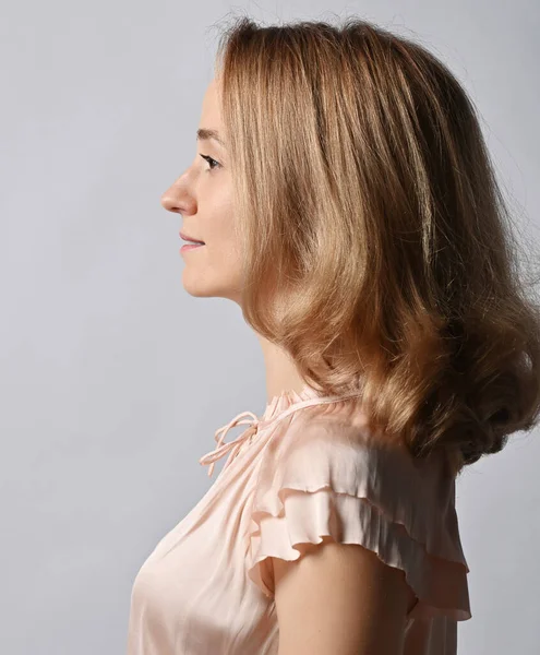 Retrato em perfil de mulher loira jovem sorridente com penteado volumétrico em blusa bege. Vista lateral — Fotografia de Stock