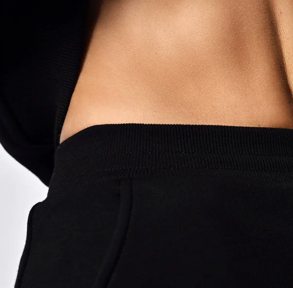 Närbild av midjan av smal kvinna i svart sportkläder luvtröja och byxor, visar hennes mage abdominals — Stockfoto