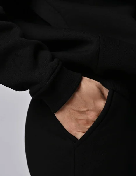 Acercamiento de la mujer en sudadera con capucha de ropa deportiva negra y pantalones de pie de lado, tomados de la mano en su bolsillo Imagen de archivo