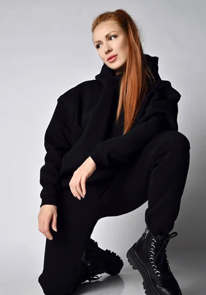 Ung fashionabla kvinna i trendiga svarta sportkläder hoodie, byxor och massiva brutala armé skor står på ett knä — Stockfoto