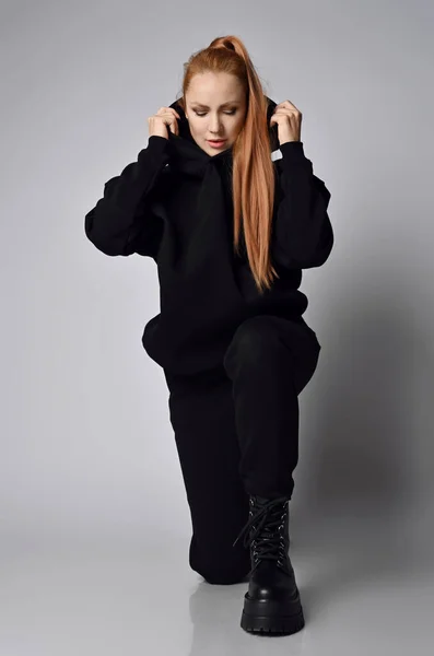 Молода струнка жінка в чорному спортивному костюмі светр, штани і масивне жорстоке армійське взуття стоїть на одному коліні — стокове фото