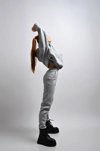 Ung smal sportig kvinna i kostym och massiva skor står sidledes hålla händerna upp, stretching. Full tillväxt — Stockfoto