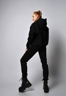 Zengin, genç, seksi, kızıl saçlı, saç örgülü, modaya uygun kapüşonlu, pantolonlu ve vahşi ayakkabılı kadın kameranın karşısında duruyor.