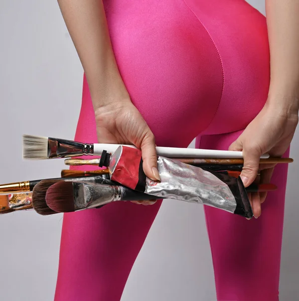 Nahaufnahme an schlanken Frauen Gesäß und Beine in rosa Leggings, halten Künstler Pinsel und Klebstoff in den Händen hinter dem Rücken — Stockfoto