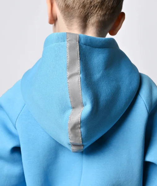 Closeup of kid boy in blue jumpsuit or hoodie standing back to camera. Shoulders, cowl with retroreflective strip Stock Photo