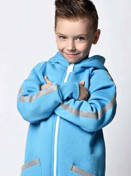 Портрет коварного улыбающегося мальчика в синем комбинезоне с капюшоном, держащего руки скрещенными на груди — стоковое фото