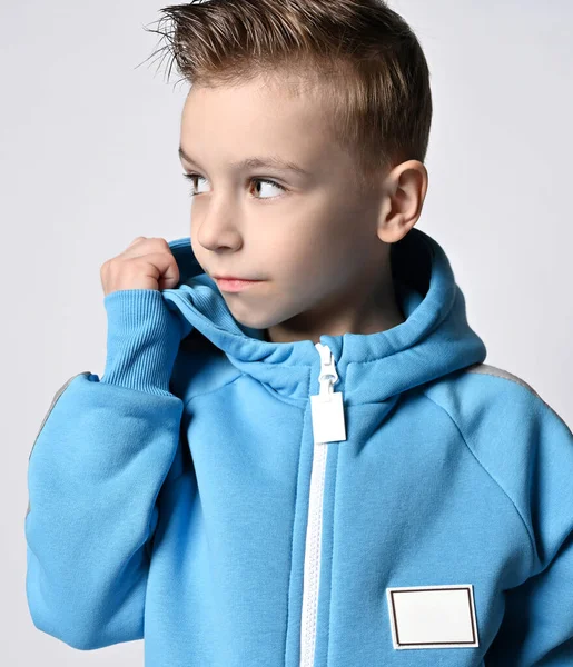 Портрет мальчика в синем комбинезоне или толстовке с молнией, стоящего с повернутой головой, смотрящего в сторону, держа свой капот — стоковое фото
