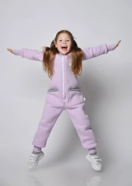 Ενεργό, frolic κορίτσι παιδί σε ροζ jumpsuit με φερμουάρ άλματα με τα πόδια και τα χέρια ανοιχτά, ευτυχισμένη ουρλιάζοντας — Φωτογραφία Αρχείου