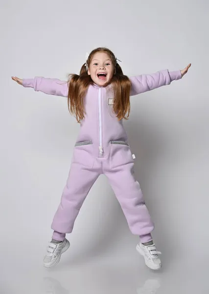 Actief, stoer meisje in roze jumpsuit met ritssluiting springt met benen en armen wijd uit elkaar, gelukkig schreeuwen Stockfoto