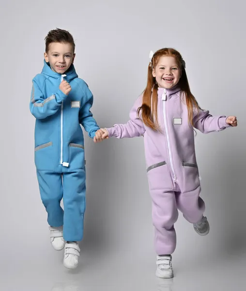 Verspielte Jungen und Mädchen in blauen und rosafarbenen Jumpsuits mit Reißverschlüssen und Taschen hüpfen und haben Spaß miteinander lizenzfreie Stockfotos