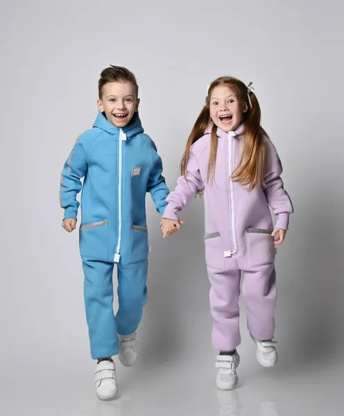 Happy laughing, frolic kids boy and girl in blue and pink jumpsuits with hoods and pockets are running together — Stock Photo, Image