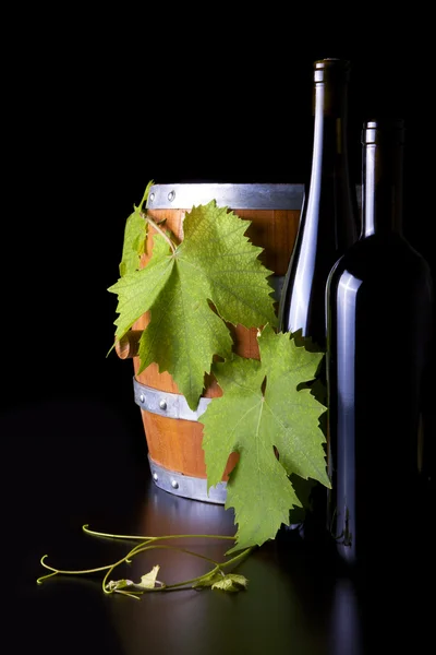 Botellas de vino, barriles y hojas de uva, fondo negro . — Foto de Stock