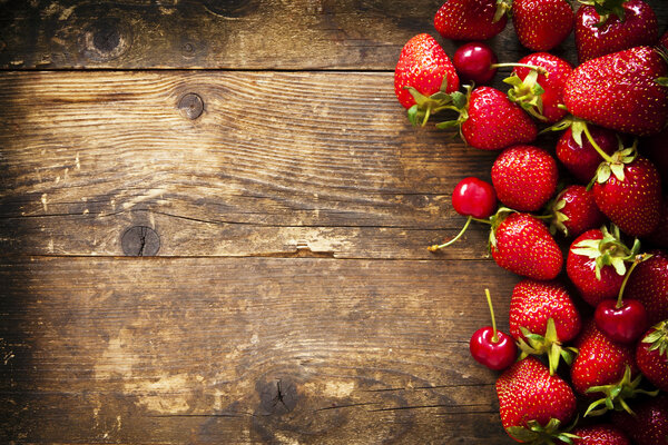 Strawberry and cherry on the old brown wooden background.