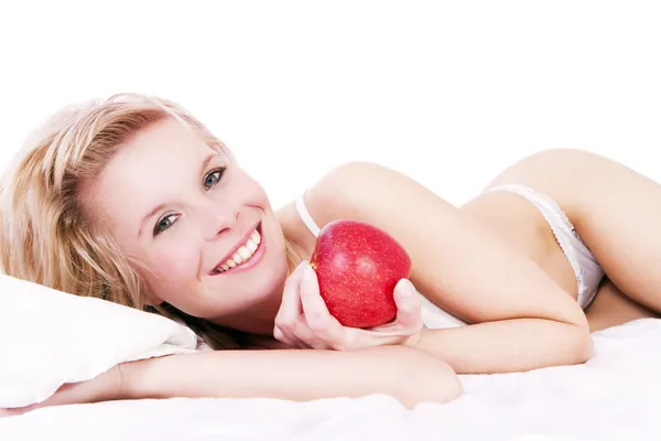 Menina loira bonita deitada na cama, segurando maçã . — Fotografia de Stock