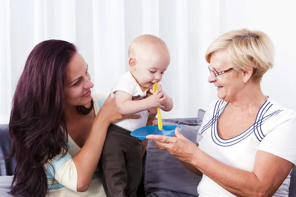 A grandmother feeding the baby with the mother. — Stock Photo, Image