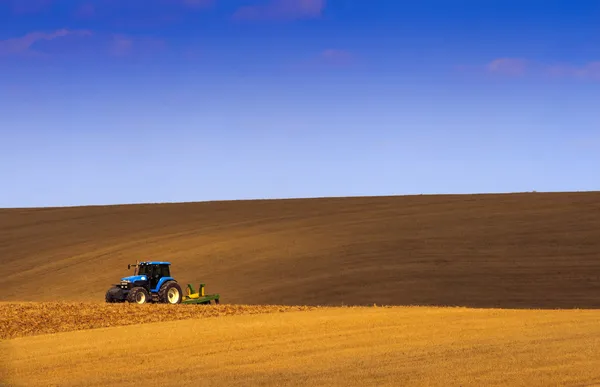 Landet av traktorn i skuggan av himmelsblå. Royaltyfria Stockfoton