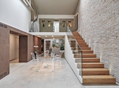 Modern bir çatı katının iç çekimleri, ön planda yemek masası sağında ahşap bir merdiven bulunan sandalyelerle duvarlar tuğlalarla kaplı.