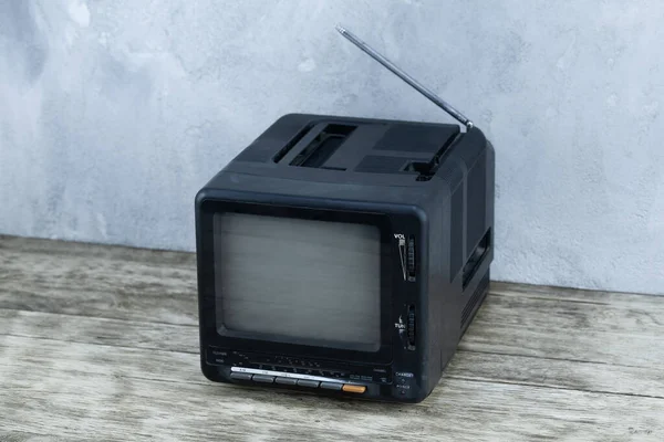 Vintage retro analog small TV set stand on wooden floor front grey concrete wall background.