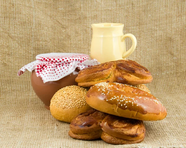 Rolls lie on sacking on a background a pot from clay and jug — Stock Photo, Image