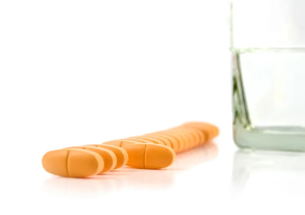 Vitamíny leží v řadě se sklenicí vody — Stock fotografie