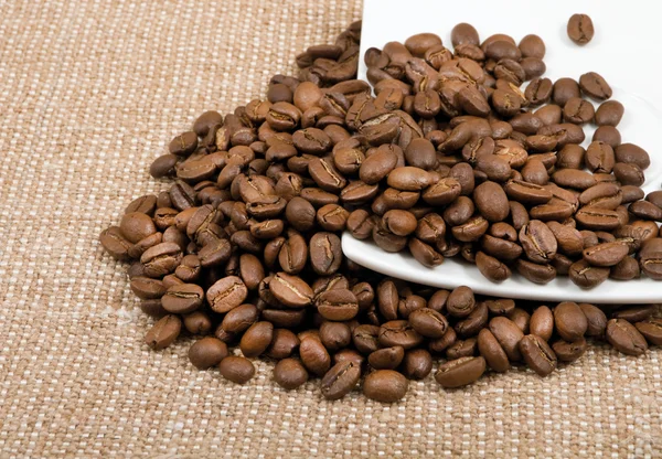 Grains of coffee lie on a saucer on a background sacking — Stock Photo, Image