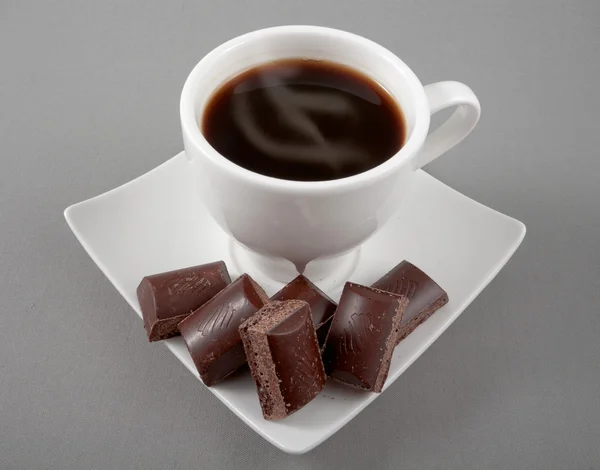 Café negro en una taza blanca y chocolate en un platillo en un gris — Foto de Stock